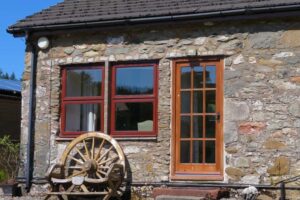 View of the entrance to the but-n-ben stone cottage with a wagin wheel and wooden bench to the side of the front door